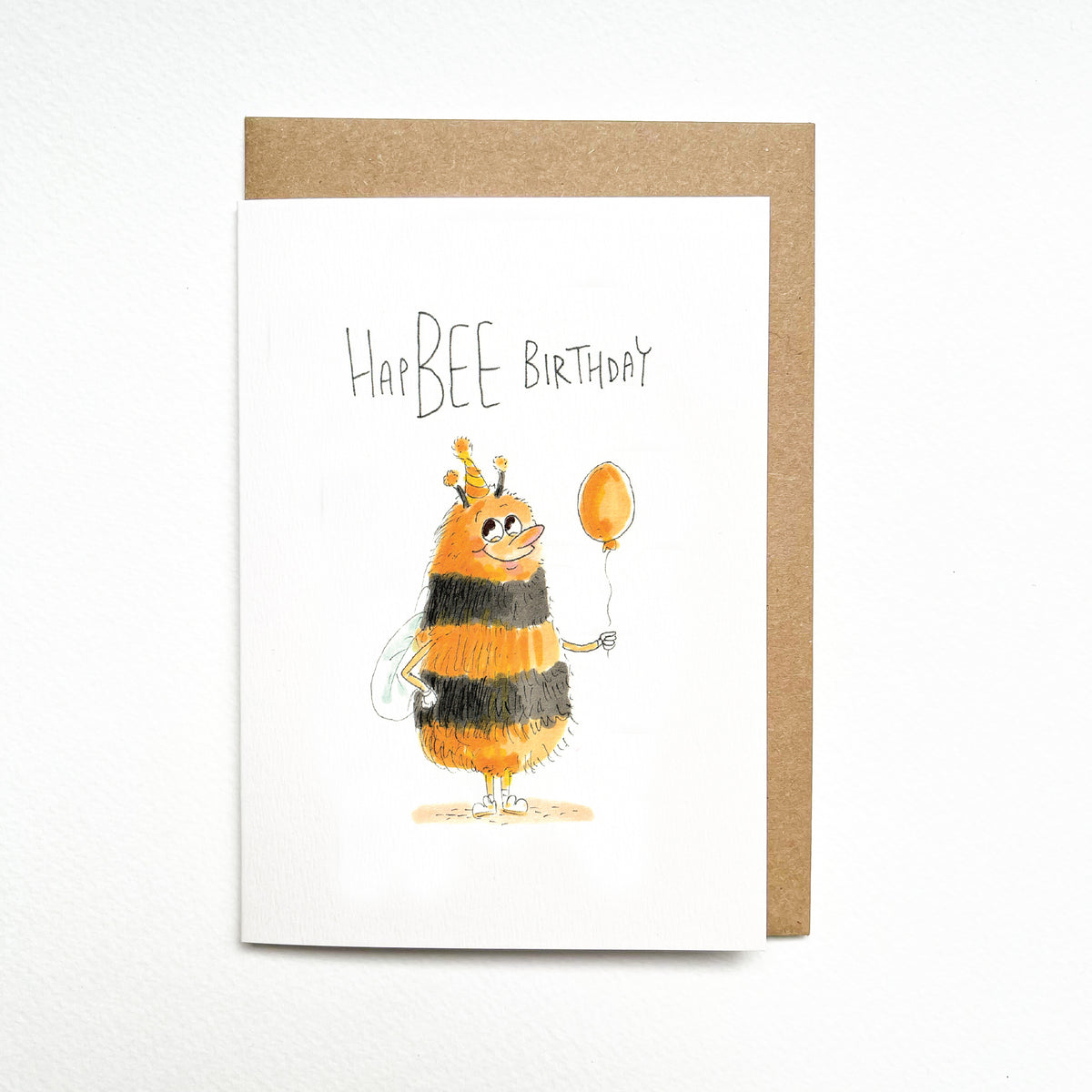 HapBEE Birthday – a fuzzy orange-and-black striped bee with delicate wings, a tiny party hat and balloon by Well Drawn Melbourne. Front product photo.