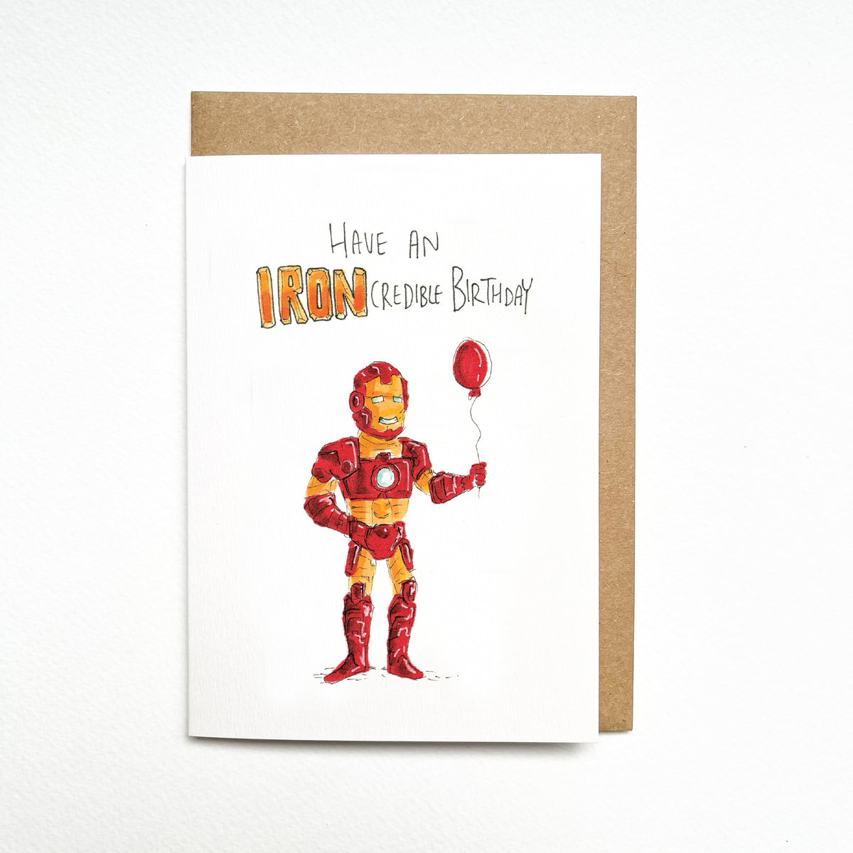 Have an IRONcredible Birthday – a red-and-gold armoured superhero holding a bright red birthday balloon by Well Drawn Melbourne. Front product photo.